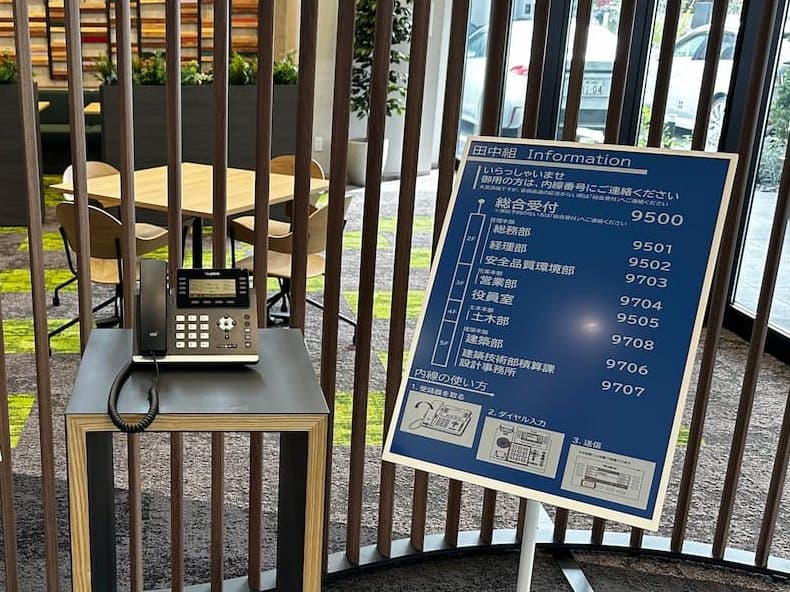 1階の受付。台の上に内線呼び出し用の電話機があり、隣に内線番号の案内板が立っている。